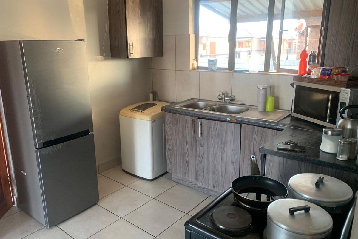 Functional kitchen featuring laminate cabinetry, tiled flooring, a double sink, and a tiled backsplash, offering a practical layout for daily meal preparation.