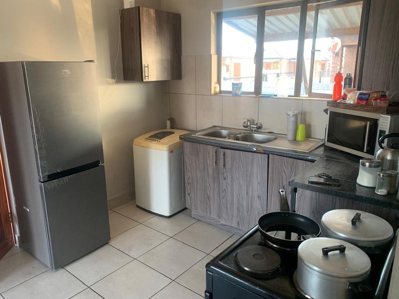 Functional kitchen featuring laminate cabinetry, tiled flooring, a double sink, and a tiled backsplash, offering a practical layout for daily meal preparation.