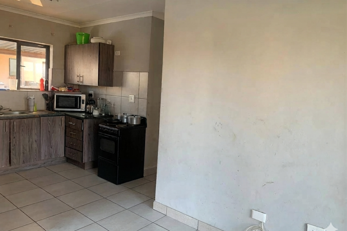 A functional kitchen area featuring wood-look cabinetry, tiled flooring, and a tiled backsplash, requiring minor cosmetic updates to the wall finishes.
