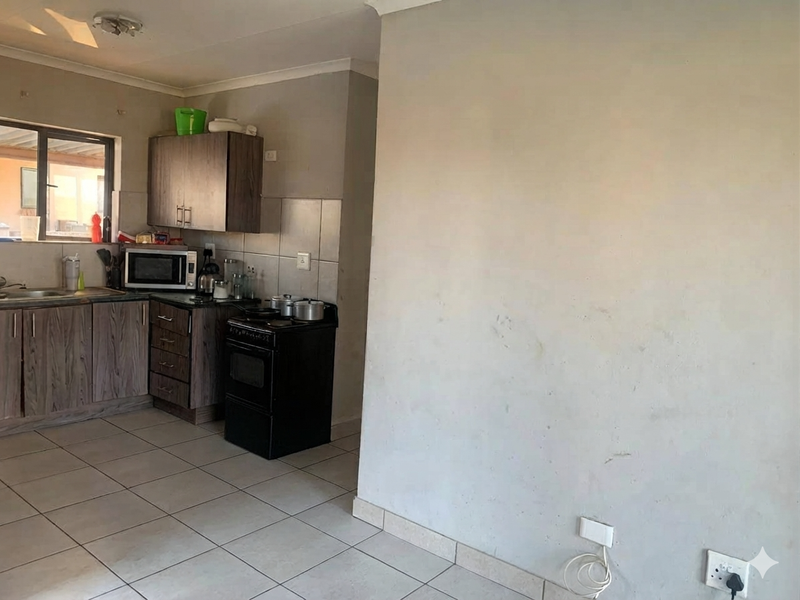 A functional kitchen area featuring wood-look cabinetry, tiled flooring, and a tiled backsplash, requiring minor cosmetic updates to the wall finishes.