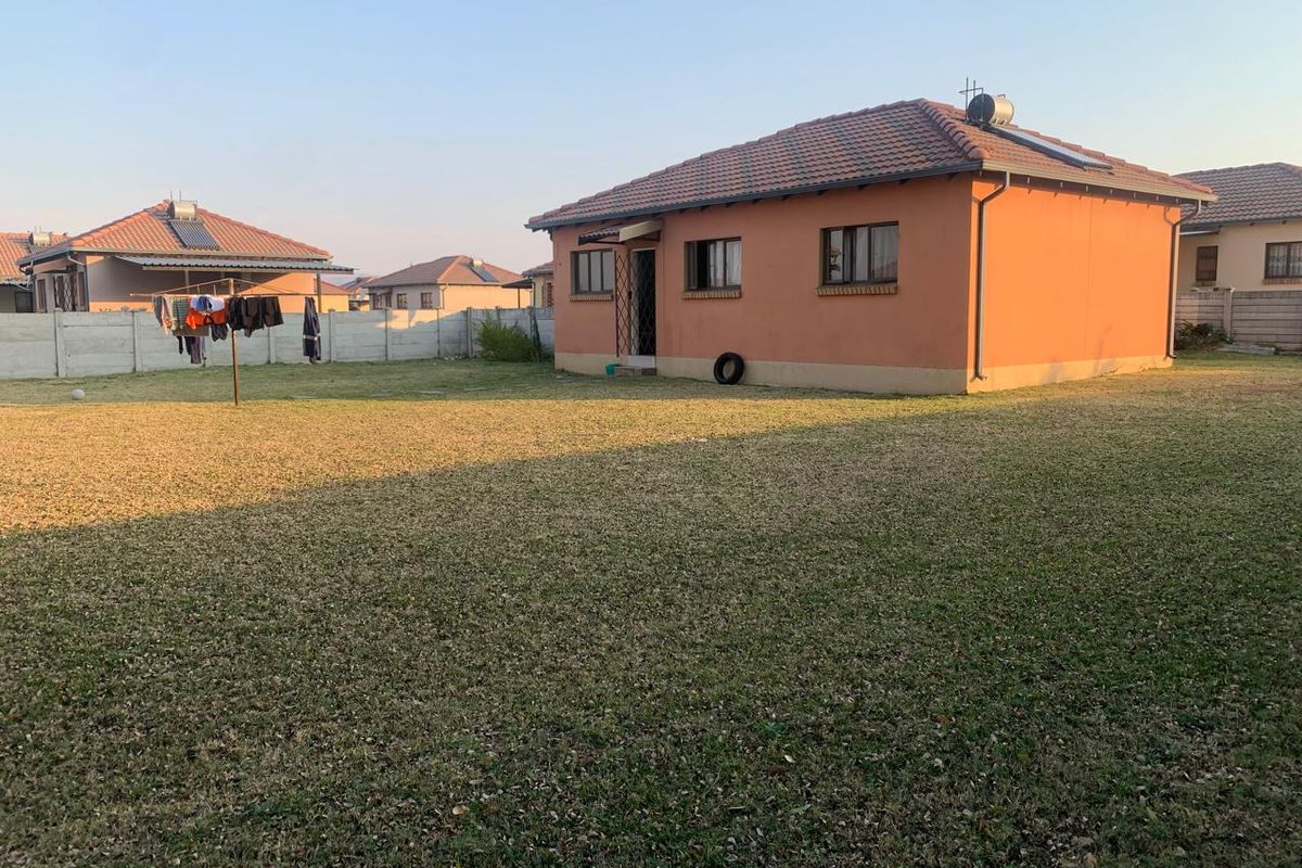 A view of the rear exterior of the townhouse, featuring a spacious lawn, tiled roof, and precast concrete boundary wall.