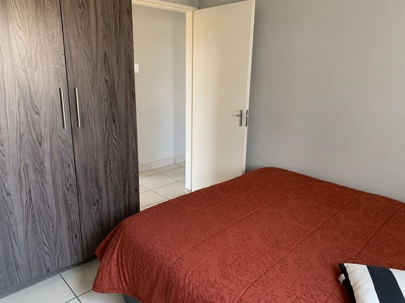 A bedroom featuring neutral wall tones, tiled flooring, and a dark wood-grain built-in wardrobe with modern handles.
