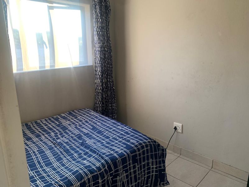 A compact bedroom featuring tiled flooring, a sliding window for natural light, and neutral wall finishes.