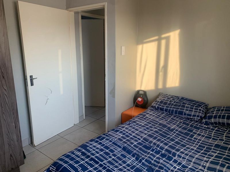 A bedroom featuring tiled flooring and a standard internal door, showing signs of wear on the door and wall surfaces.