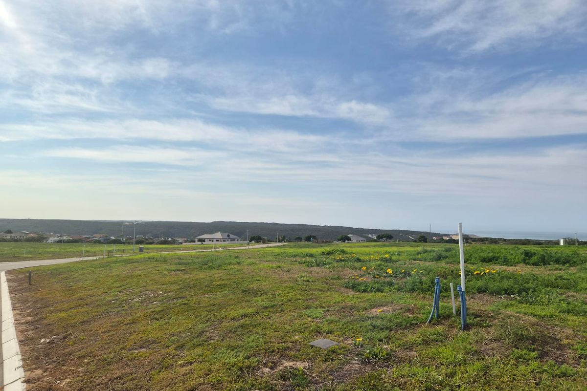A vacant residential plot featuring established utility connection points, paved road access, and scenic coastal landscape views.
