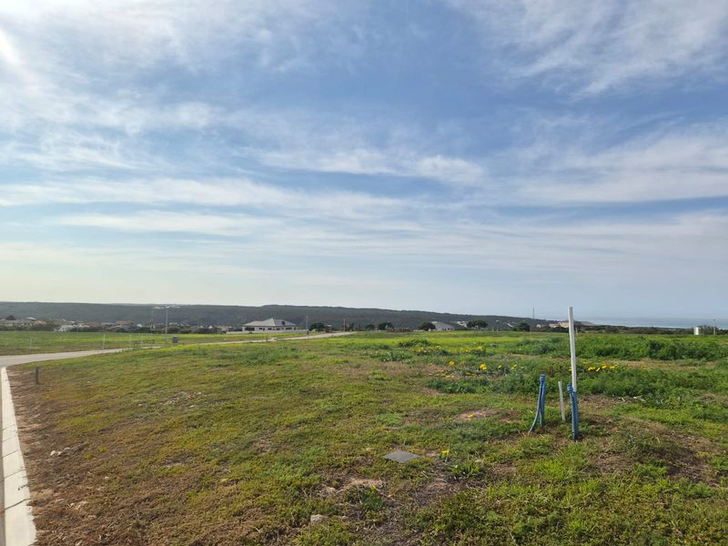 A vacant residential plot featuring established utility connection points, paved road access, and scenic coastal landscape views.