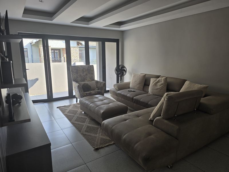 Modern living room featuring tiled flooring, recessed ceiling detail, and large aluminium stacker doors providing access to the outdoor area.