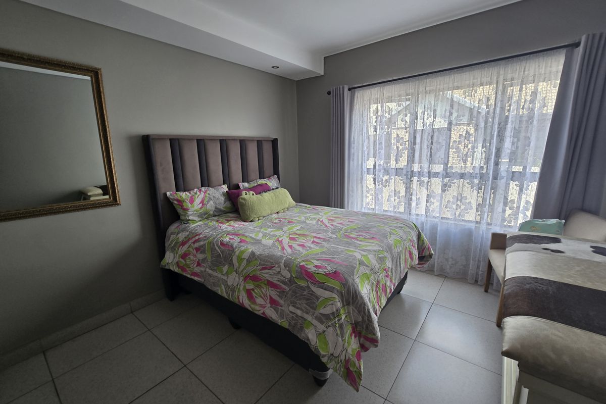 A well-lit bedroom featuring neutral wall tones, tiled flooring, and a large window that allows for ample natural light.