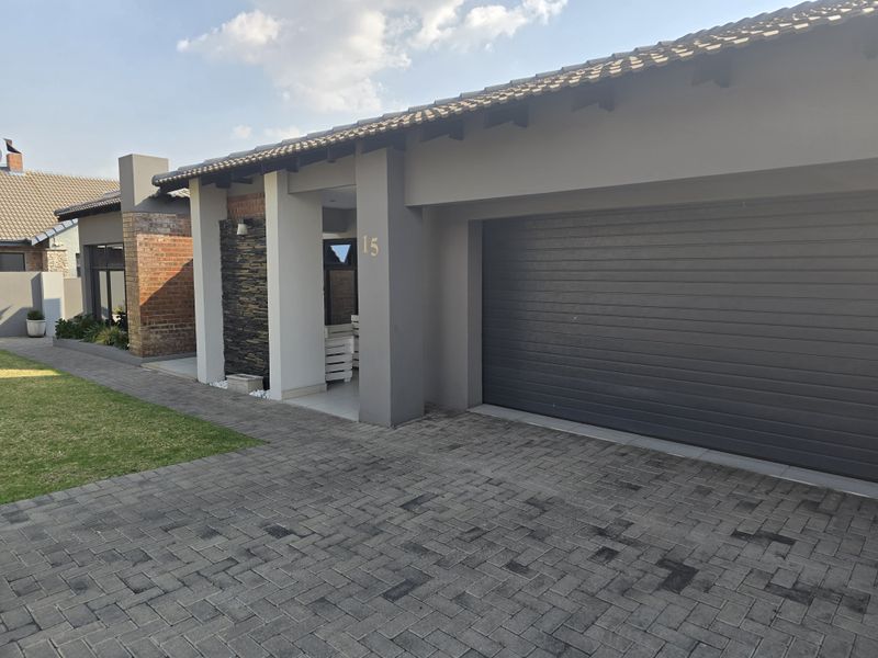 Modern front facade featuring a paved driveway, sectional garage door, and a stylish stone-clad entrance pillar.