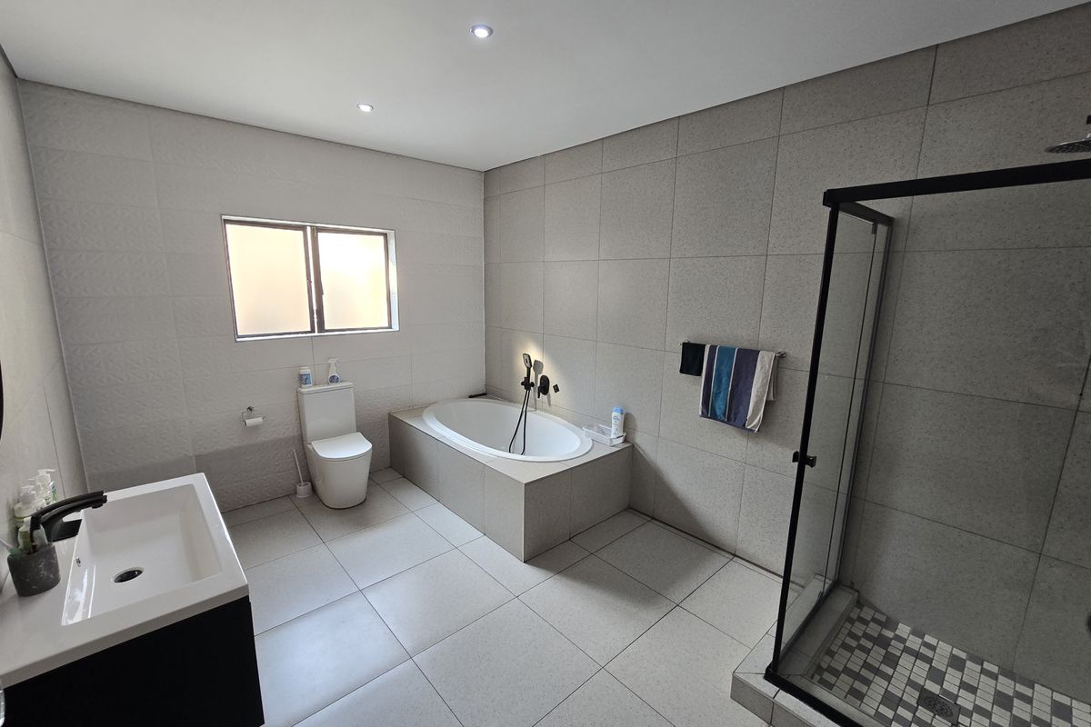 Modern bathroom featuring a built-in bathtub, separate walk-in shower, vanity basin, and neutral floor-to-ceiling tiling with recessed lighting.