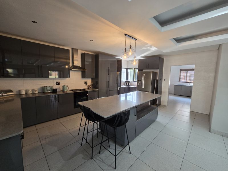 Modern kitchen featuring high-gloss cabinetry, a central stone-topped island, integrated appliances, and recessed ceiling lighting, with an adjacent scullery area.