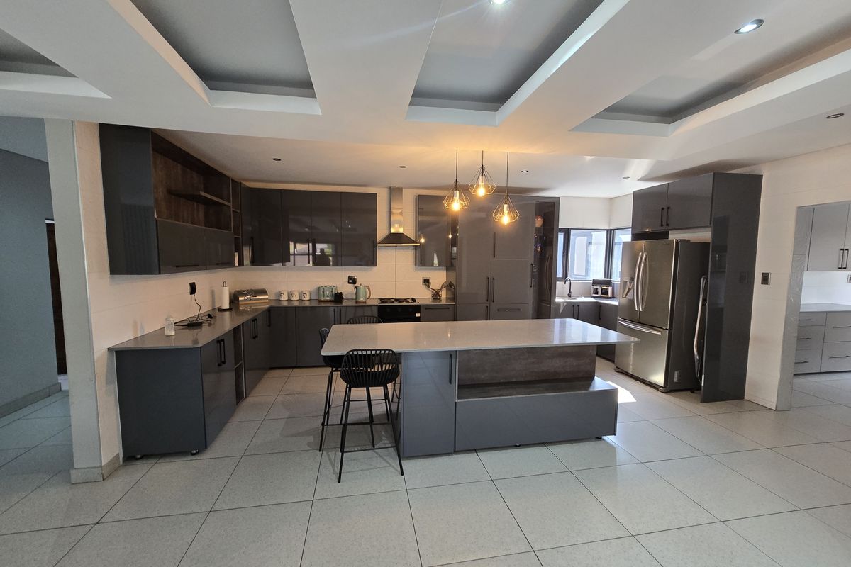 Modern kitchen featuring dark grey cabinetry, a central island with stone countertops, recessed ceiling lighting, and tiled flooring.