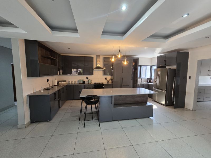 Modern kitchen featuring dark grey cabinetry, a central island with stone countertops, recessed ceiling lighting, and tiled flooring.