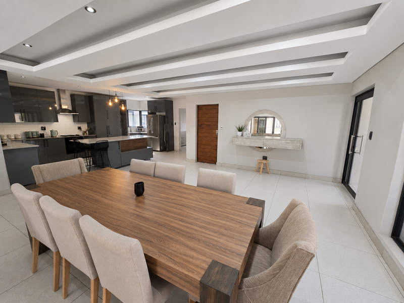 Spacious open-plan living and dining area featuring a modern kitchen with island, coffered ceilings, recessed lighting, and large format floor tiles.