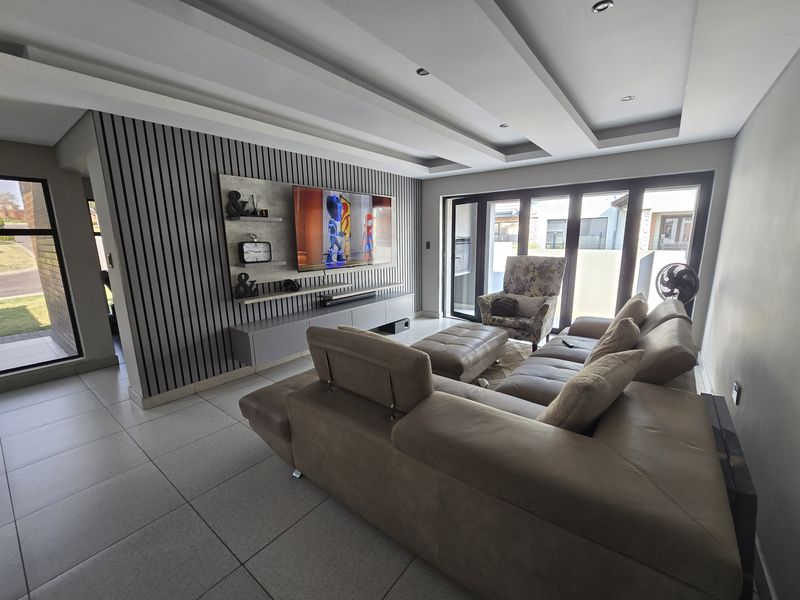 Modern living room featuring a stylish slatted timber feature wall, recessed ceiling with integrated lighting, large tiled floors, and expansive bi-fold doors to the exterior.