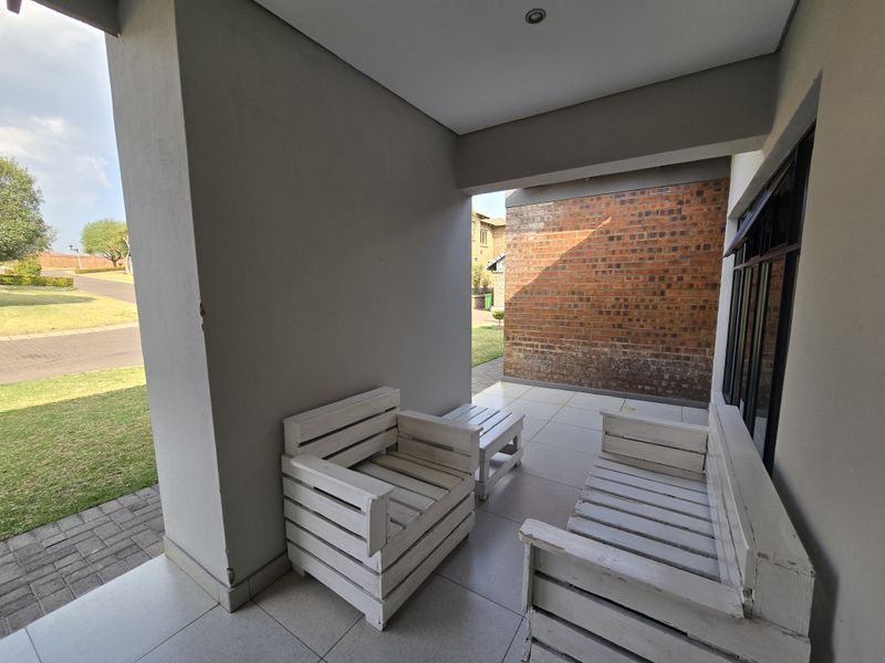 A covered patio area featuring tiled flooring, recessed lighting, and an exposed brick wall, providing a pleasant outdoor space for relaxation.