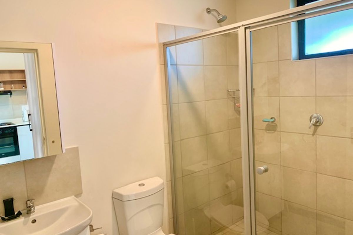 A functional bathroom featuring a glass-enclosed shower, pedestal basin, and toilet with neutral wall and floor tiling.