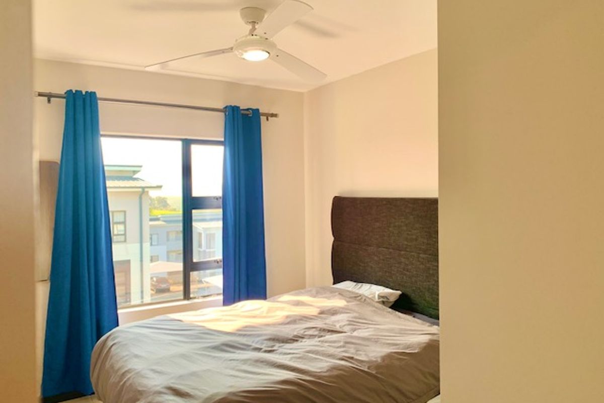 A well-lit bedroom featuring a ceiling fan and large aluminium-framed windows, offering a bright and comfortable living space.