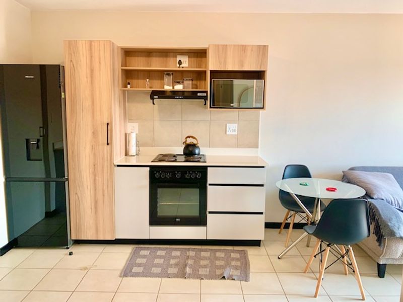 Compact open-plan kitchen featuring modern light wood and white cabinetry, integrated oven, hob, and extractor fan, seamlessly flowing into the living area.