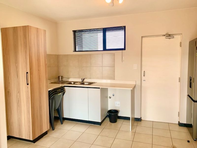 A functional kitchen area featuring built-in cabinetry, a stainless steel sink, tiled backsplash, and neutral tiled flooring.