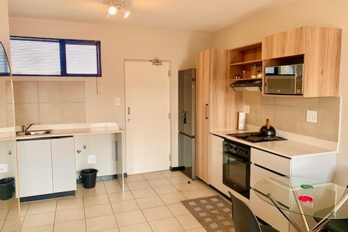 Functional kitchen featuring light wood-tone cabinetry, tiled backsplash, built-in oven, hob, and extractor fan with ample counter space and tiled flooring.