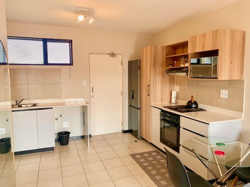 Functional kitchen featuring light wood-tone cabinetry, tiled backsplash, built-in oven, hob, and extractor fan with ample counter space and tiled flooring.