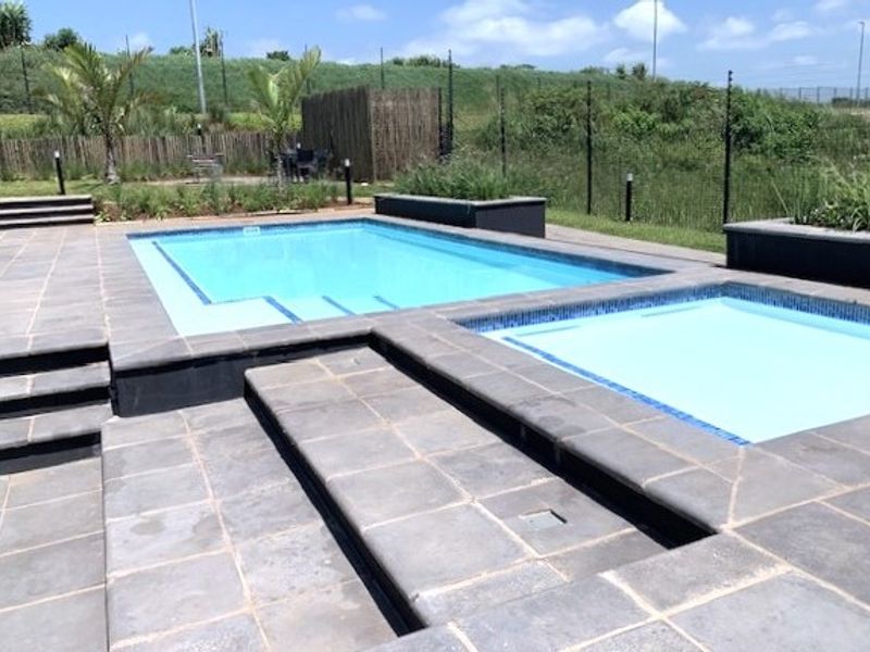 A well-maintained outdoor swimming pool area featuring tiled surrounds, raised planter boxes, and integrated steps, set within a fenced garden environment.