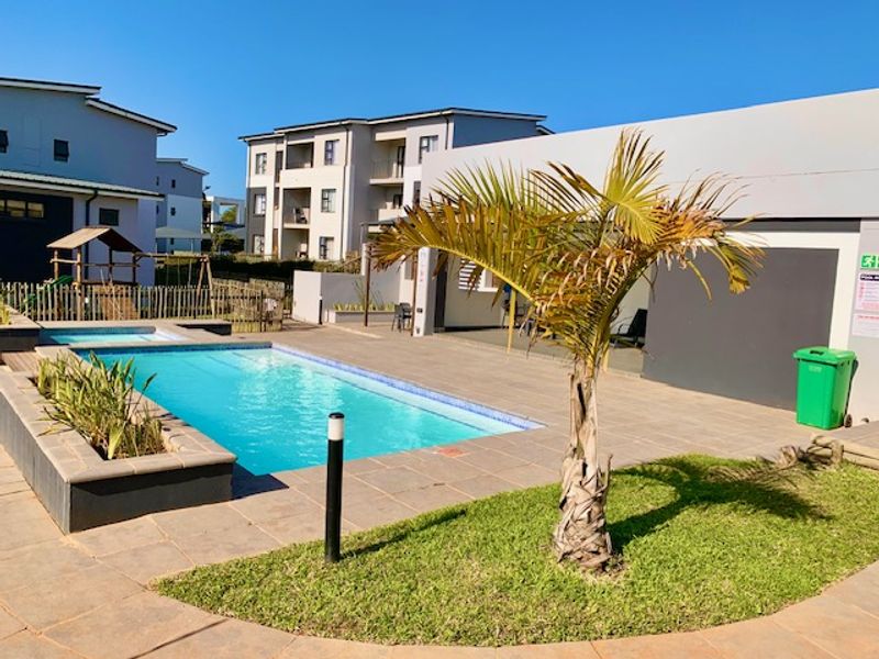 A well-maintained communal swimming pool area featuring a tiled deck, raised planter beds, and landscaped surroundings within an apartment complex.