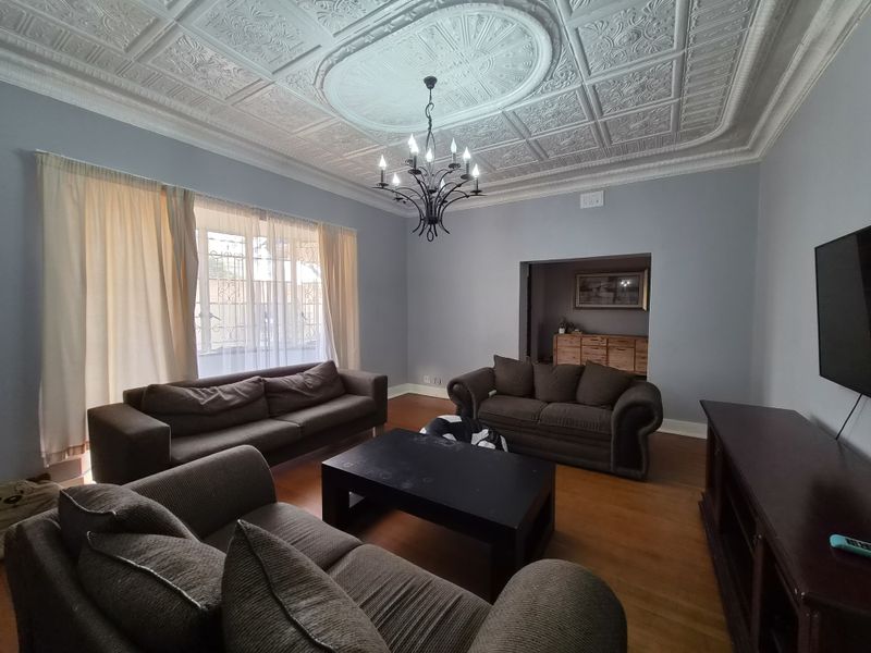 Spacious living room featuring a decorative pressed metal ceiling with a central rose, hardwood flooring, and large windows with security bars.