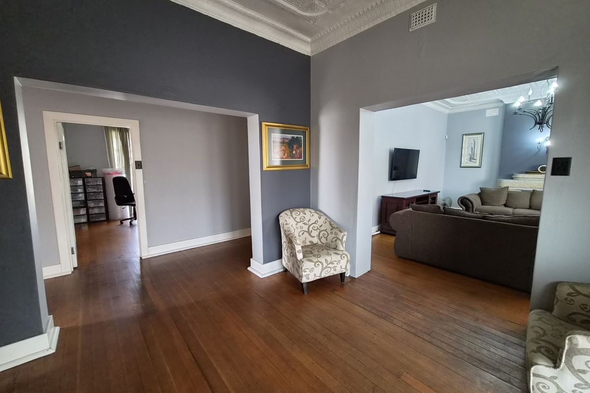 Spacious living area featuring original hardwood flooring and an ornate pressed metal ceiling, connecting to adjacent rooms through wide archways.