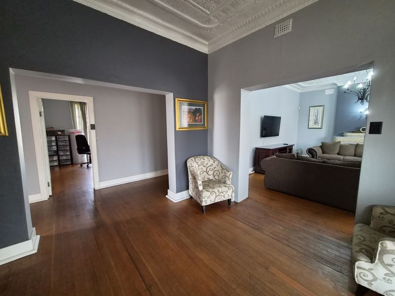 Spacious living area featuring original hardwood flooring and an ornate pressed metal ceiling, connecting to adjacent rooms through wide archways.