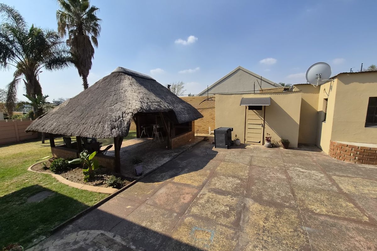 Rear exterior view featuring a traditional thatch lapa, paved patio area, and established garden space, offering potential for outdoor entertainment.