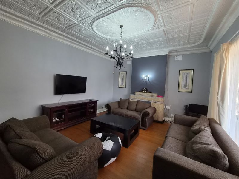 Spacious living room featuring a decorative pressed metal ceiling with a central rose, hardwood flooring, and a fireplace surround.