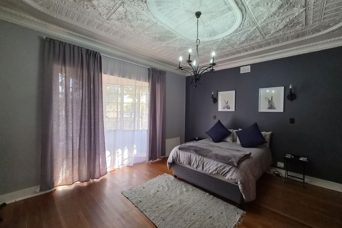 Spacious bedroom featuring a classic ornate pressed metal ceiling, polished hardwood flooring, and elegant dark feature wall.
