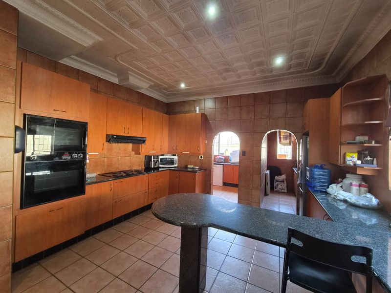 Spacious kitchen featuring extensive wooden cabinetry, granite countertops, a breakfast bar, built-in oven, and a distinctive coffered ceiling with tiled finishes.