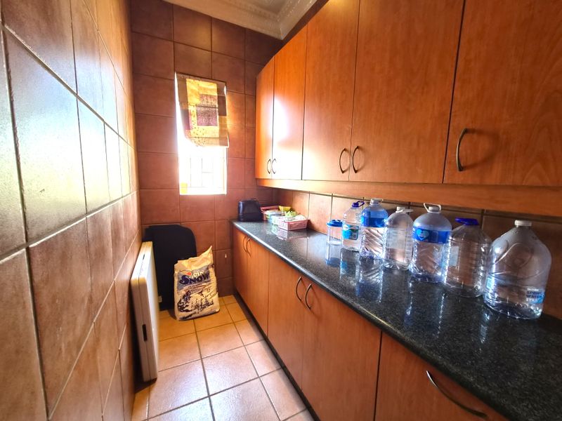 A functional scullery featuring extensive built-in wooden cabinetry, granite countertops, and full-height ceramic wall tiling.