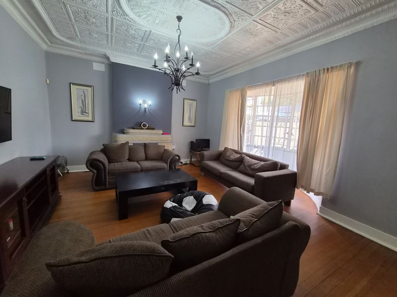 Spacious living room featuring a decorative pressed metal ceiling, original hardwood flooring, and a classic fireplace mantle with elegant lighting fixtures.