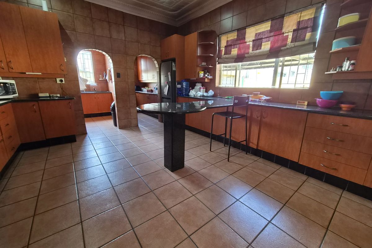 Spacious kitchen featuring extensive wooden cabinetry, granite countertops, a breakfast bar, and tiled finishes throughout, with an adjoining scullery area.