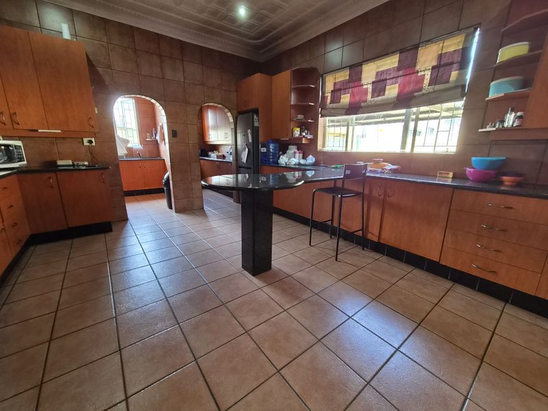 Spacious kitchen featuring extensive wooden cabinetry, granite countertops, a breakfast bar, and tiled finishes throughout, with an adjoining scullery area.
