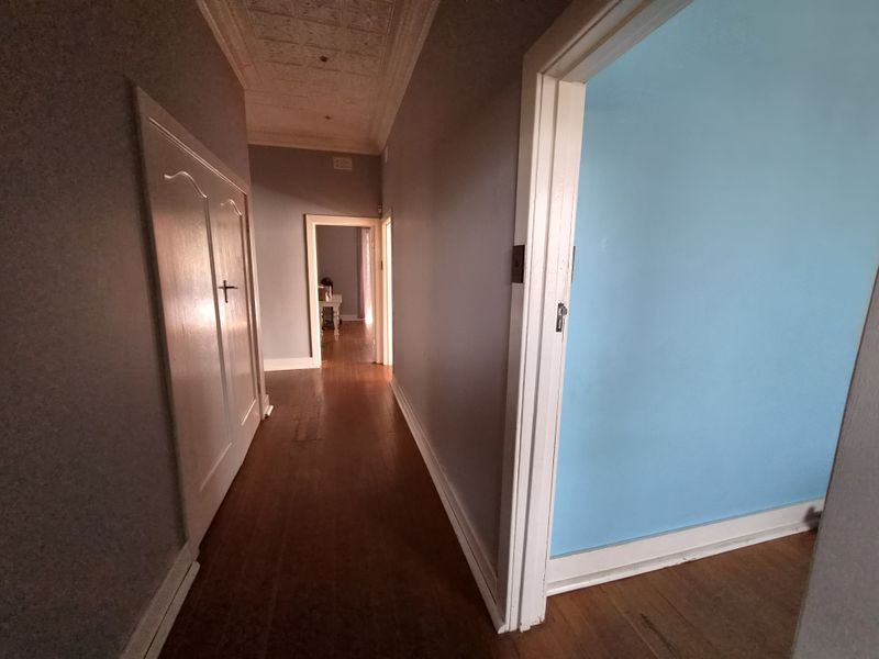 A spacious hallway featuring original timber flooring and a decorative pressed metal ceiling, connecting multiple rooms throughout the home.