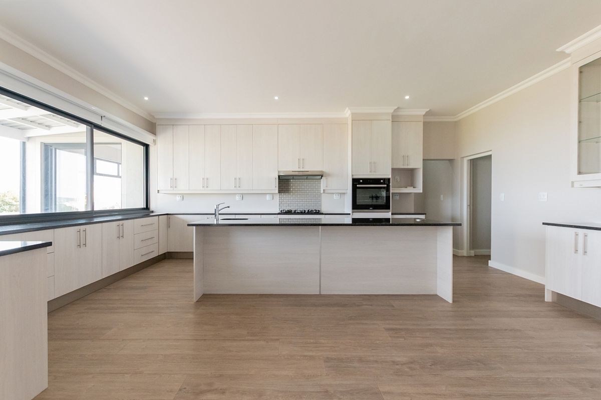 Modern, spacious kitchen featuring light wood cabinetry, a central island with stone countertops, built-in appliances, and durable laminate flooring.