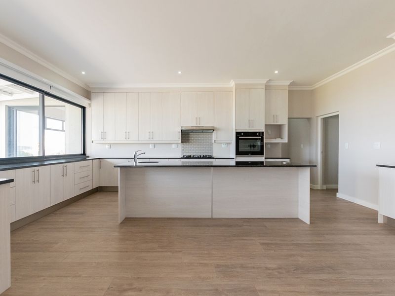 Modern, spacious kitchen featuring light wood cabinetry, a central island with stone countertops, built-in appliances, and durable laminate flooring.