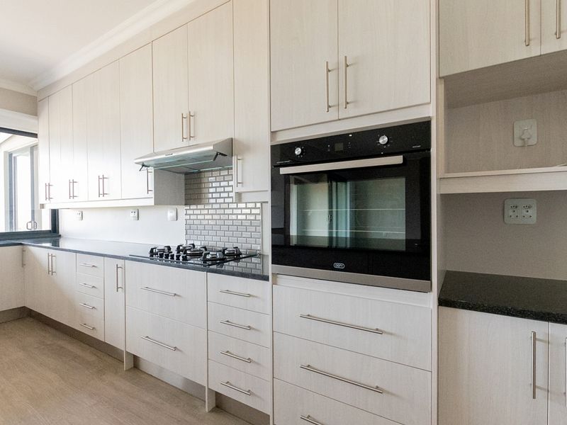 Modern kitchen featuring light wood cabinetry, stone countertops, subway tile backsplash, and integrated appliances including a gas hob and built-in oven.