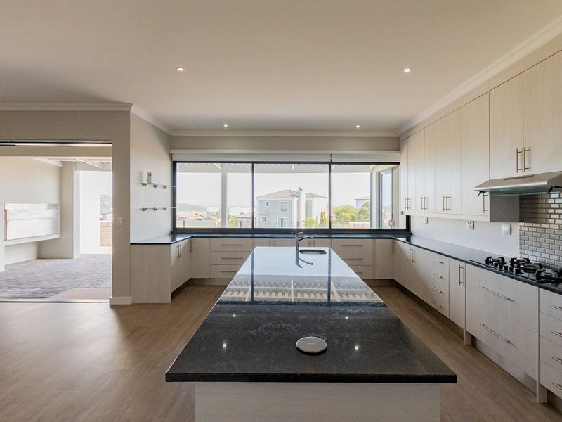 Modern, spacious kitchen featuring a large central island with granite countertops, ample built-in cabinetry, gas hob, and integrated extractor fan.