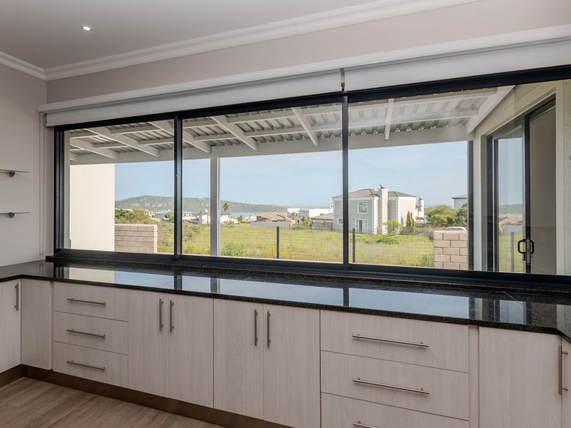 Modern kitchen area featuring sleek built-in cabinetry, granite countertops, and a large sliding window offering expansive views of the surrounding neighborhood.