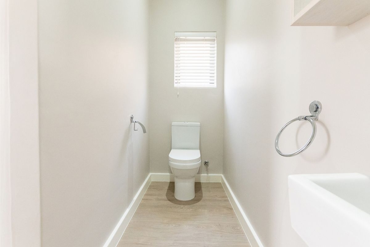 A clean and modern guest bathroom featuring a white toilet, wall-mounted basin, and light wood-look laminate flooring.