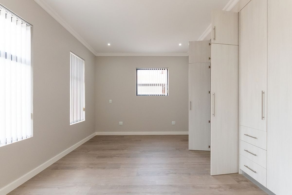 A bright, empty bedroom featuring light-toned laminate flooring, neutral walls, recessed lighting, and extensive built-in cabinetry with modern finishes.