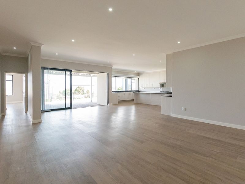 Spacious open-plan living and kitchen area featuring modern laminate flooring, recessed lighting, and large sliding doors leading to an outdoor patio.