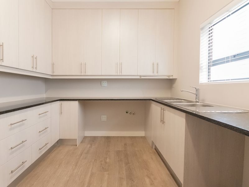 A clean and modern laundry room featuring ample built-in cabinetry, laminate countertops, a stainless steel sink, and dedicated plumbing connections.