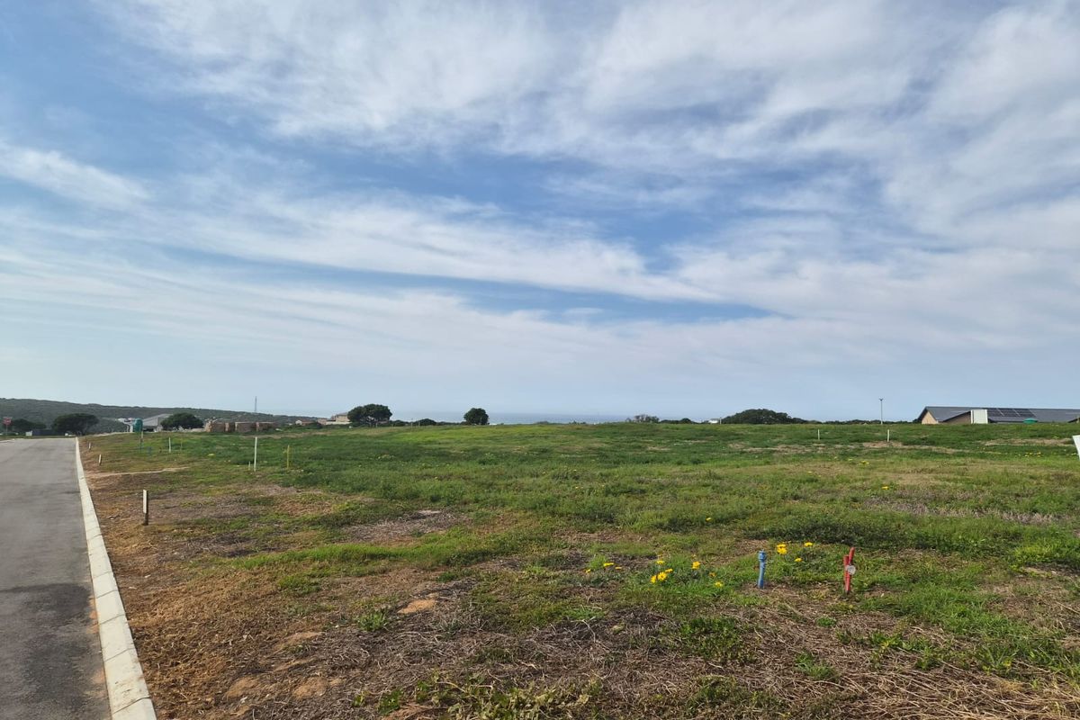 A vacant residential plot featuring a level grassy landscape, paved road access, and visible utility connection points, offering potential for new construction.